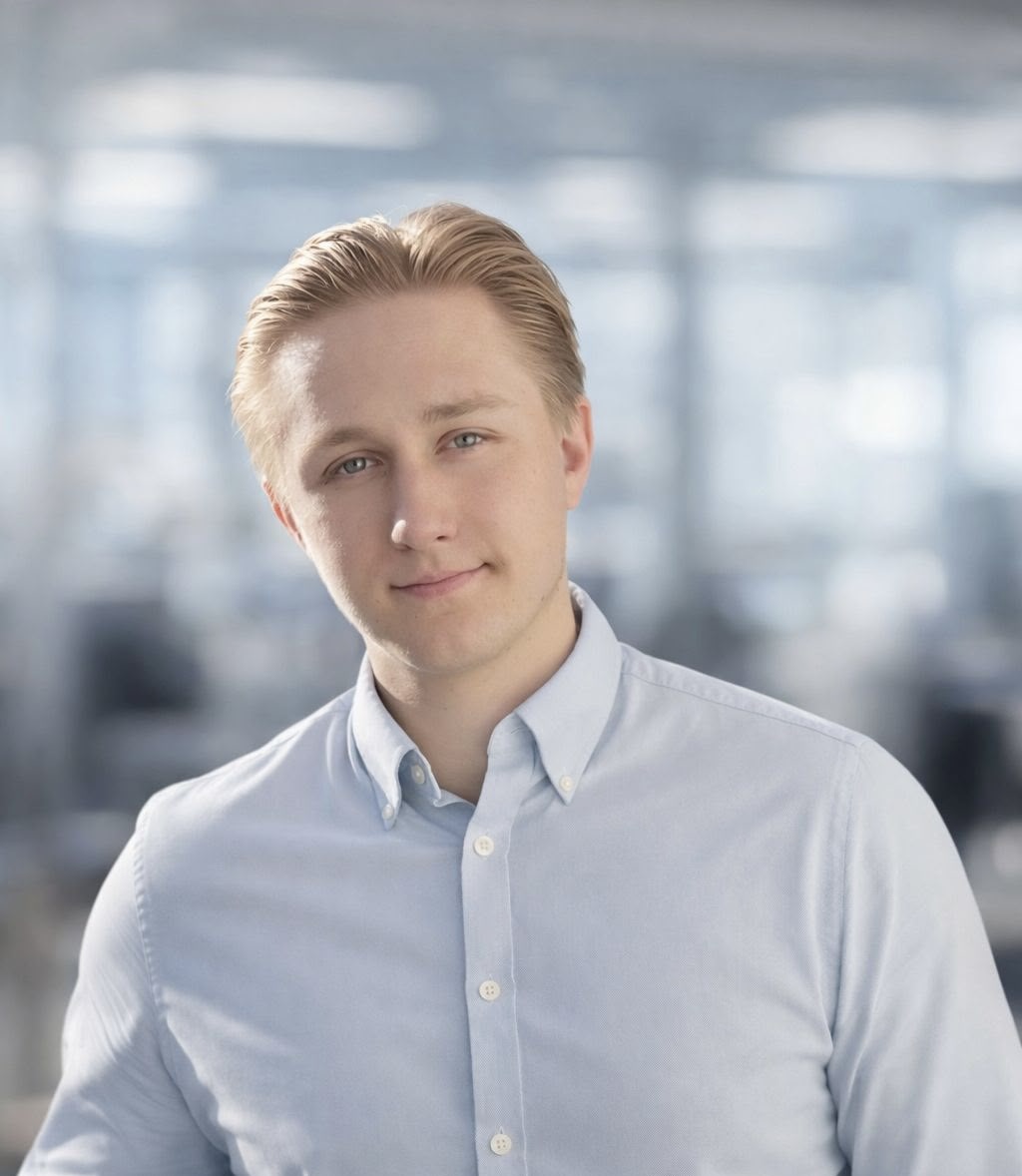 Das Bild zeigt Benjamin Dahler vor einem bewegten Hintergrund. Er trägt ein hellblaues Hemd und kurze blonde Haare.