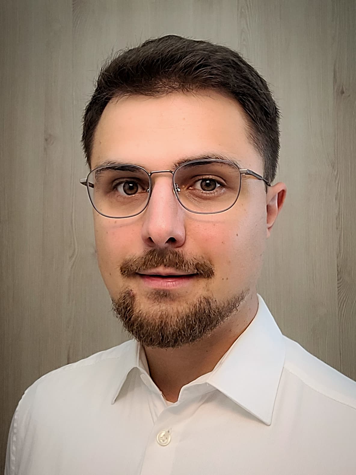 Das Bild zeigt Rune Betz. Er trägt ein weißes Hemd, Drei-Tage-Bart, eine schwarze Brille und kurzes, dunkelbraunes Haar
