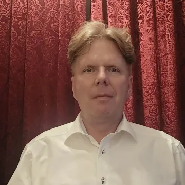 Das Bild zeigt Ingo Gering vor einem roten Hintergrund. Er trägt ein weißes Hemd und kurze blonde Haare.